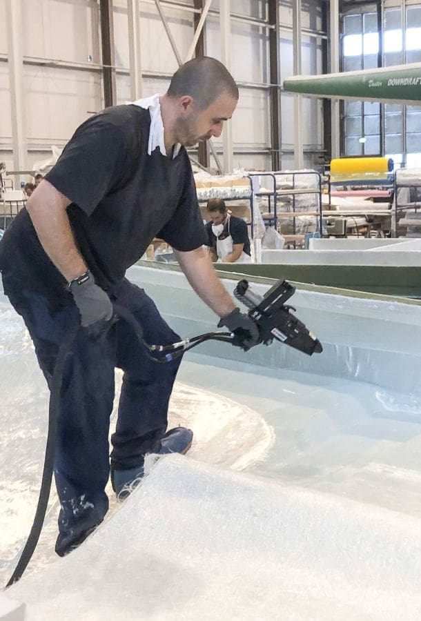 Man using the Vactac system to apply hot melt adhesive to the fiberglass layer on a boat hull