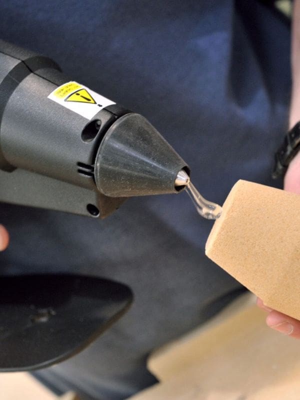 Industrial sized hot melt glue gun applying hot melt to a sand casting
