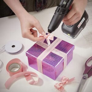 Small cordless glue gun being used to bond a pink bow to a present box.